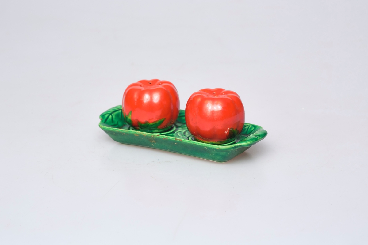 Salt- og pepperbøsse har motiv og farge som en tomat. Fatet (a) er grønt og har motiv av blad.