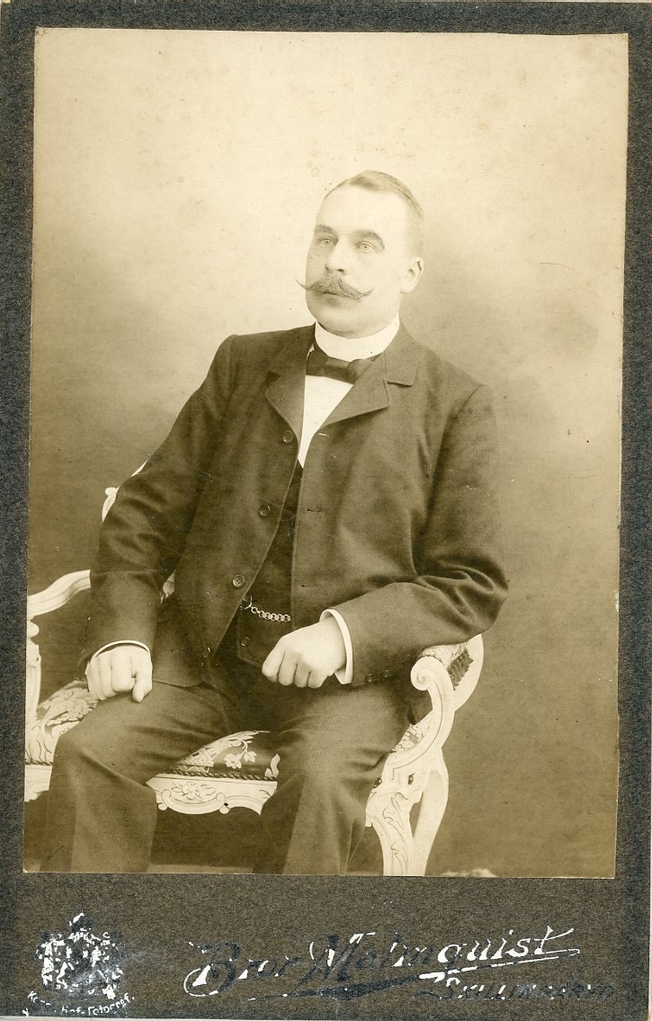 Kabinettsfotografi av en okänd man med spetsig mustasch som sitter i en stol.