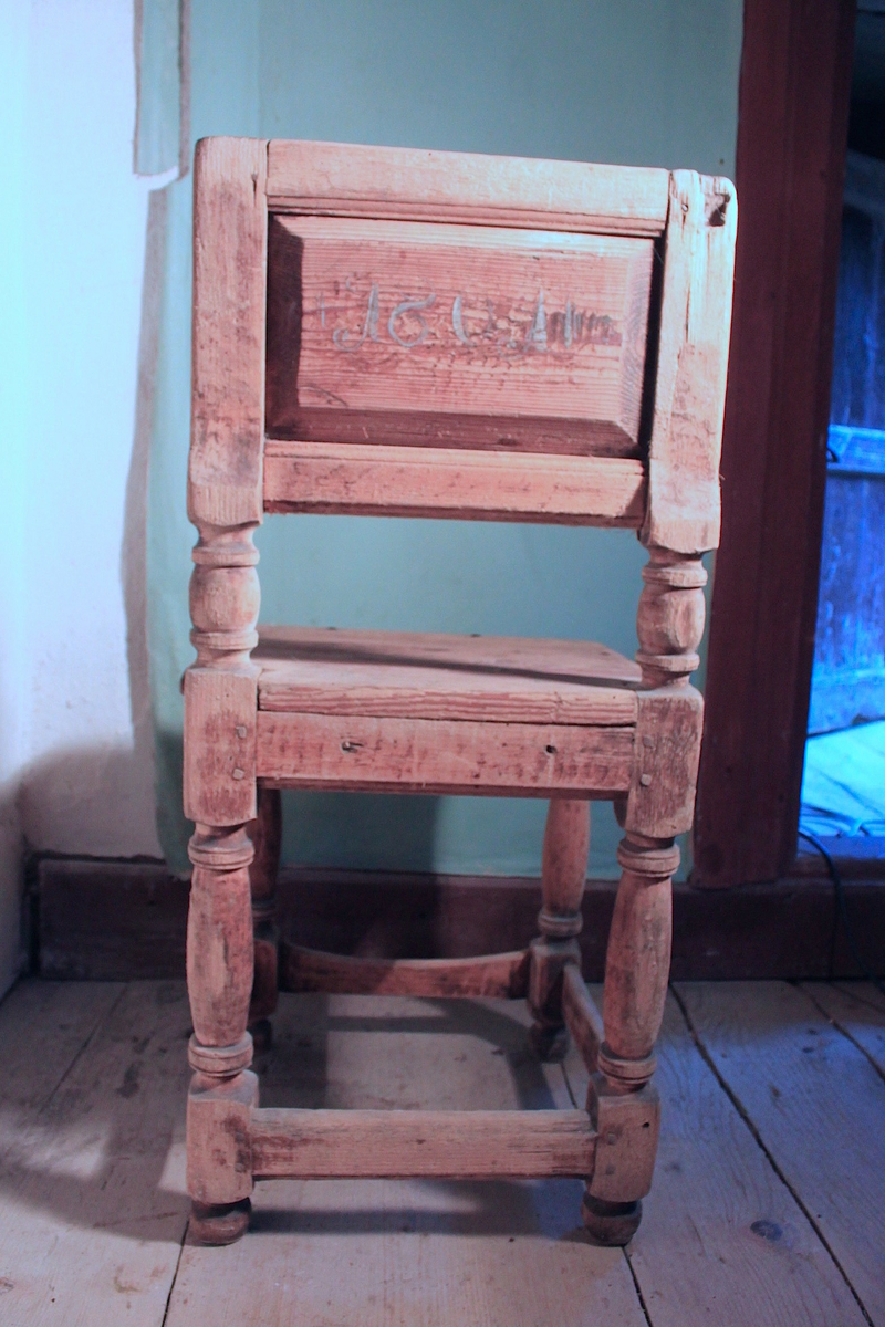 Stol av trä. Fyra svarvade ben med tvärslåar. Ryggstödet är två svarvade stolpar med en hel infälld träplatta. Framsidan  målad i rött med svart dekormålning. Baksidan skrivet datum, 1801, inramat med lodräta sträck och liggande S i turkos eller blått.