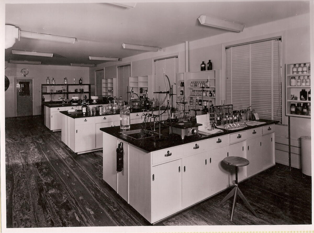 Sort-hvitt-bildet viser et laboratorium med tre benker som står ut fra veggen.