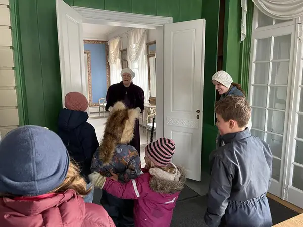 Barn i vintertøy blir møtt av en to museumsansatte i kostyme i døra til fru Ankers leilighet. Den ene er kledd som tjenestejente, den andre som fru Anker.