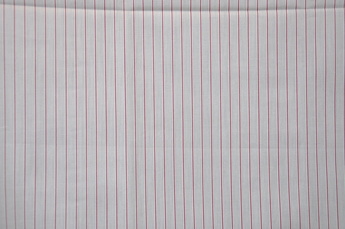 Bomullstyg, 1940-tal. 
Skjorttyg på 80 cm bredd, poplin. 2-färgstryck i mörkrosa och grått; 1 smal rand och 5 smalare ränder i grupp.
Otvinnat garn.
Sanforiserat.