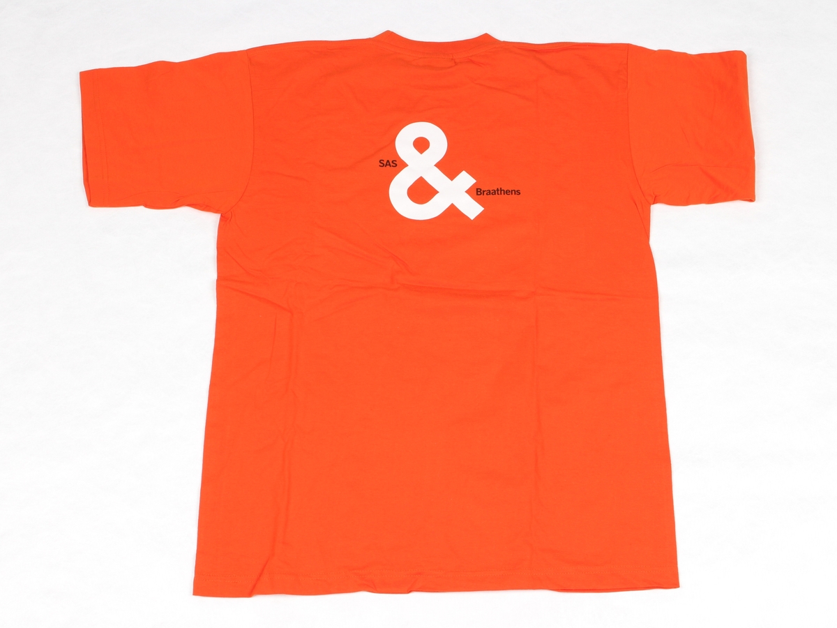 Oransje t-skjorte med rund hals. Liten SAS Braathens-logo på brystet, og større motiv på ryggen. Størrelse L.