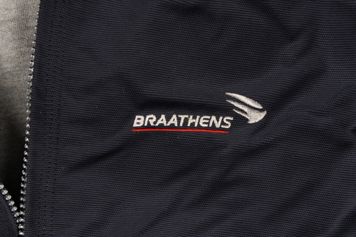 Mørk blå høstjakke med 4 lommer og hette som kan foldes inn i lomme i nakken. Brodert Braathens vinge-logo på brystet og brodert slagord på høyre lomme. Størrelse L.