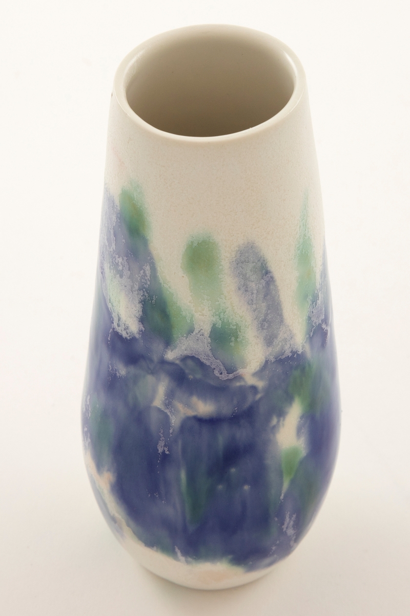Blank hvit, balusterformet porselensvase med åpen munning. Brede strøk med blå og grønn glasur på korpus. Enkelte krystaller i glasuren.