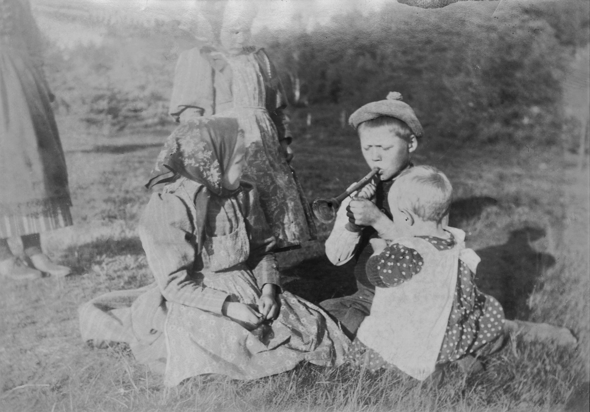 Barnen i Dammstugan leker utomhus. Gottfrid blåser i trumpet för systrarna Anna till höger, Edit och ytterligare en flicka.