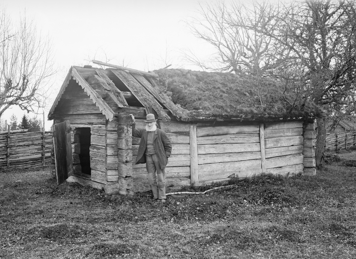 Ålderdomlig badstuga på gården Fundshult i Svinhults socken. Dokumenterad 1904. Den gamle mannens identitet har inte kunnat styrkas.