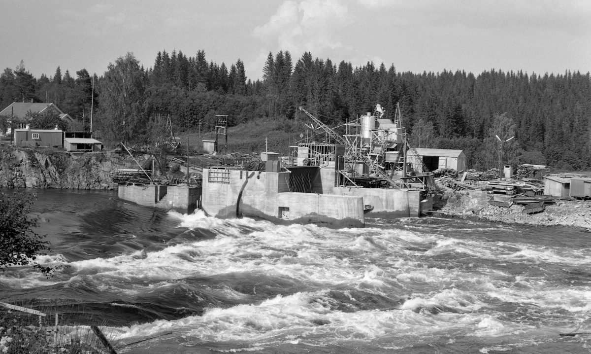 Anleggsarbeid ved Svanfossdammen i Vorma i 1961. Dette anlegget ligger i Fenstand i Nes på Øvre Romerike. Etter at jernbanen mellom Kristiania og Eidsvoll sto ferdig, med dampskipsforbindelse videre nordover mjøsbyene, var det behov for å heve vannspeilet i elva fra endestasjonen og oppover mot Minnesund. I slutten av 1850-åra ble dette løst ved at det ble reist en dam ved Sundfossen. Den første reguleringsdammen ved Svanfossen sto ferdig i 1910.  I 1958 lanserte Glommen og Laagens Brukseierforening planer for et nytt damanlegg ved Svanfossen. Planen var å bygge en dam som kunne heve vannspeilet med 75 centimeter og dermed bruke kunne bruke mjøsvann til å tilføre den nedenforliggende delen av vassdraget når det var for lite vann der. Arbeidet ved Svanfossen i 1958 startet med sprenging av en tunnel i fjellet på vestsida av elveløpet som skulle gi bedre avløp ved lav vannføring. Den nye demningen ble bygd cirka 15 meter nedenfor den gamle. Den fikk fire sektorluker av stål. Lukene kunne heves eller senkes. Luka i tømmerløpet kunne senkes så langt at tømmeret kunne flyte over lukas overkant. De øvrige kunne heves over vannspeilet når det var behov for å slippe mer vann nedover i vassdraget.
