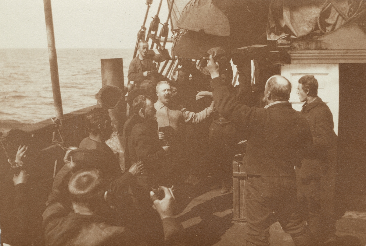 Fotografi från första svenska Antarktisexpeditionen 1901-1904. Motiv av expeditionsdeltagare och besättningsmän som skålar ombord på ett fartyg.