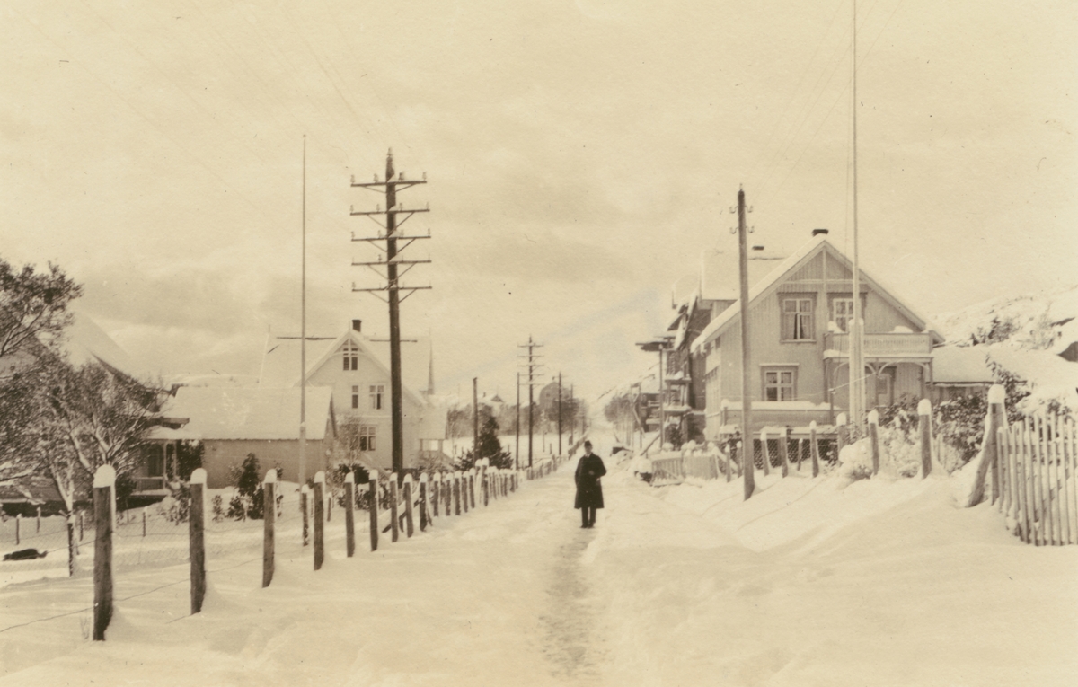 Fotografi från Albin Ahrenbergs resa till Grönland 1929. Motiv av telefonstolpar och man på snötäckt gata i liten stad.