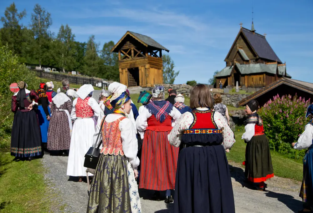 Gruppe kvinner i bunad foran en stavkirke