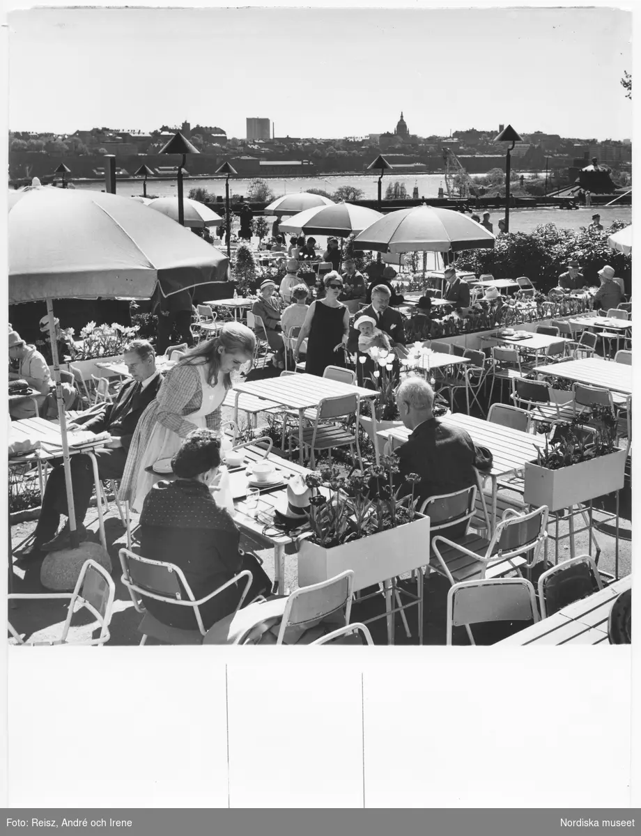Stockholm. Solliden på Skansen, bord med gäster och uppfällda parasoller. En servitris plockar disk hos gästerna i förgrunden.