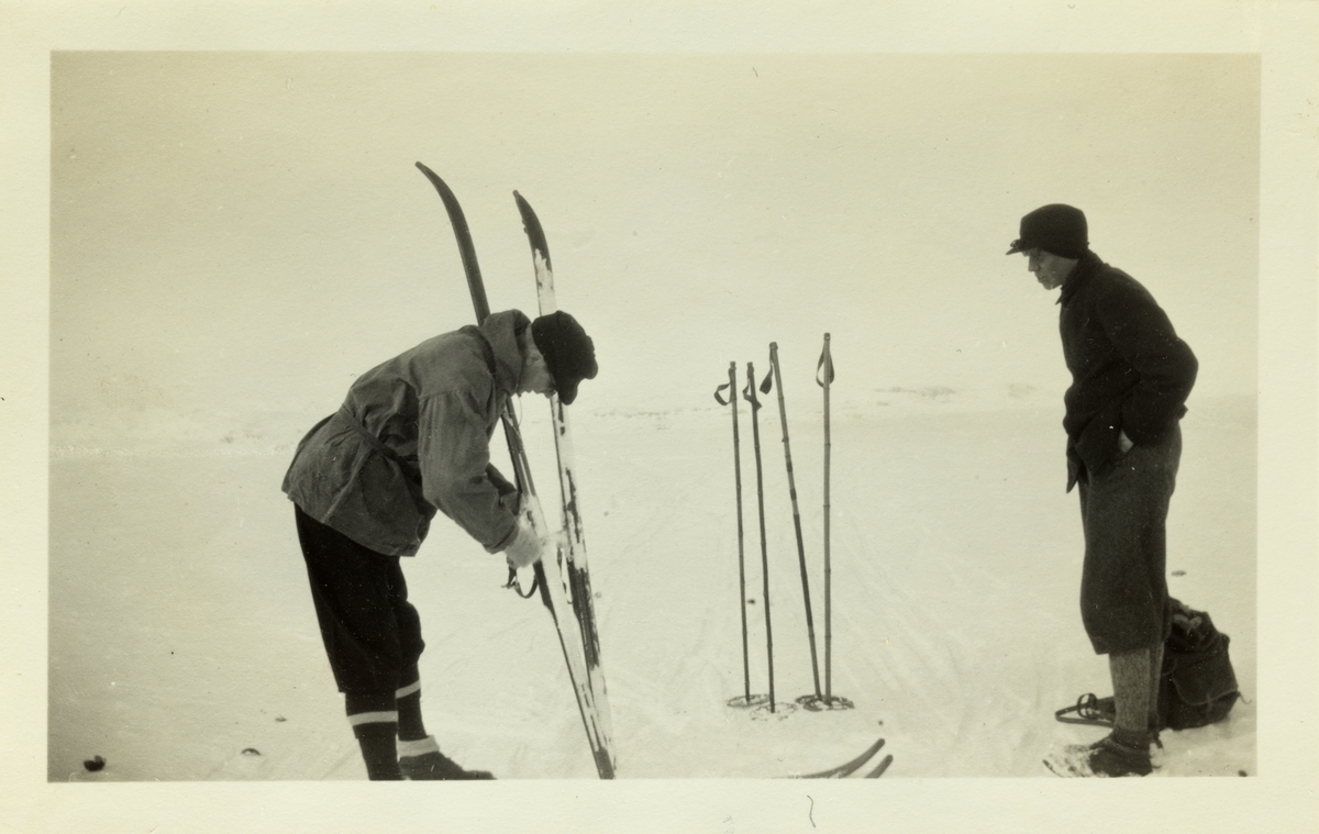 To menn, hvorav den ene smører ski, på skitur på Hardangerjøkulen i påsken 1928.