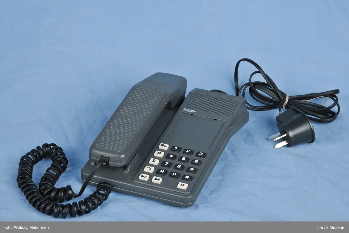 Tastafon TELE. Tastatur på høyre side bord. Telefon i holder venstre side.