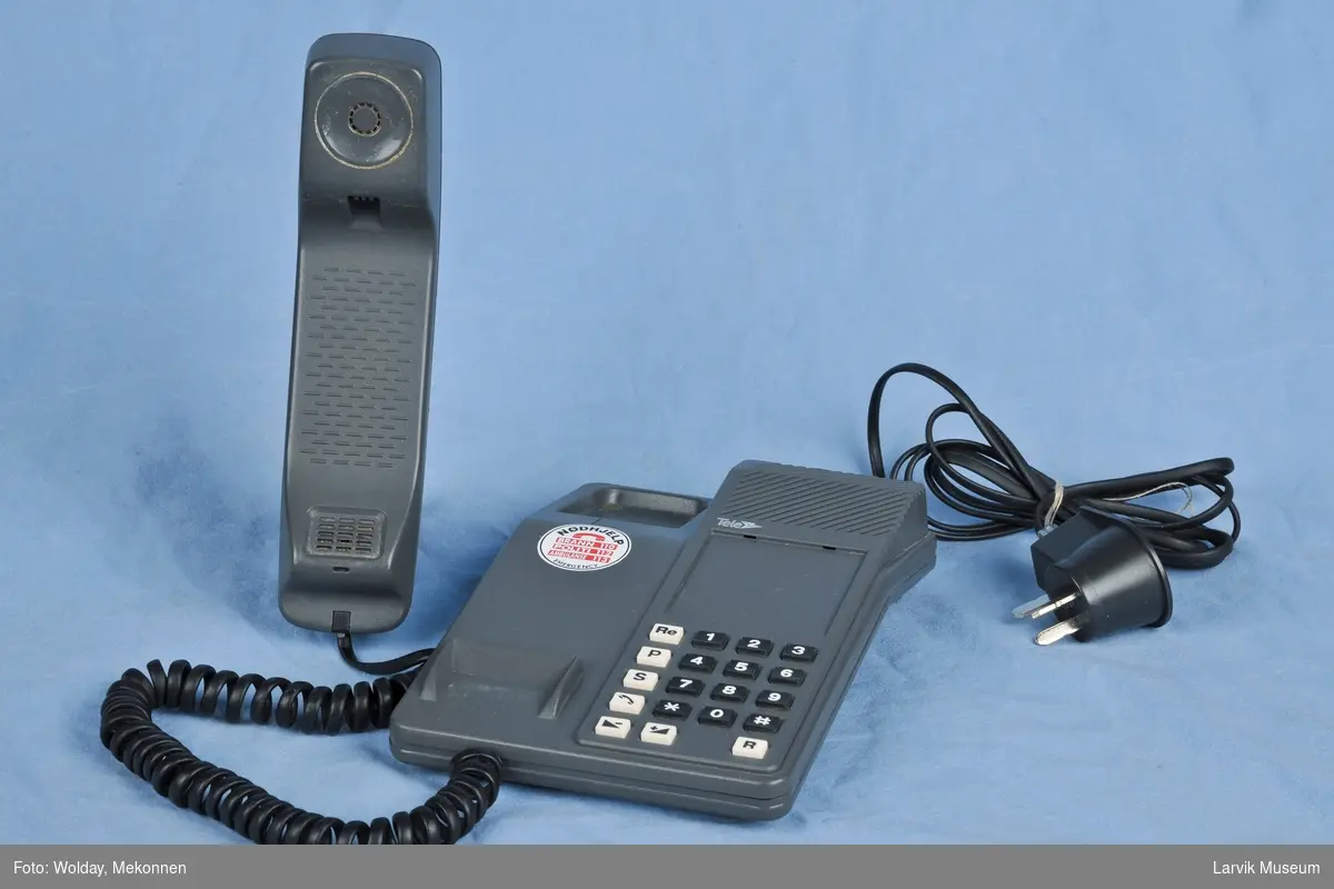 Tastafon TELE. Tastatur på høyre side bord. Telefon i holder venstre side.