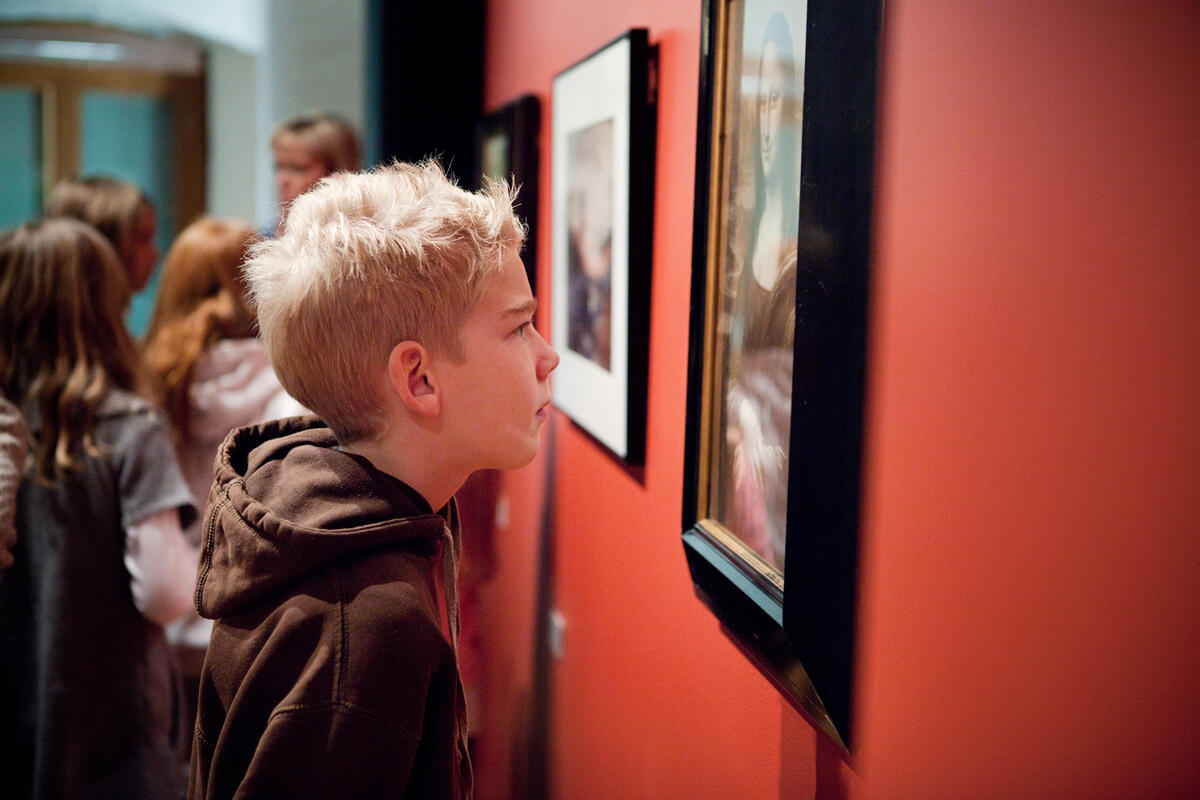 En gutt studerer et bilde på en rød vegg. Bildet er fra lokalene Preus museum.