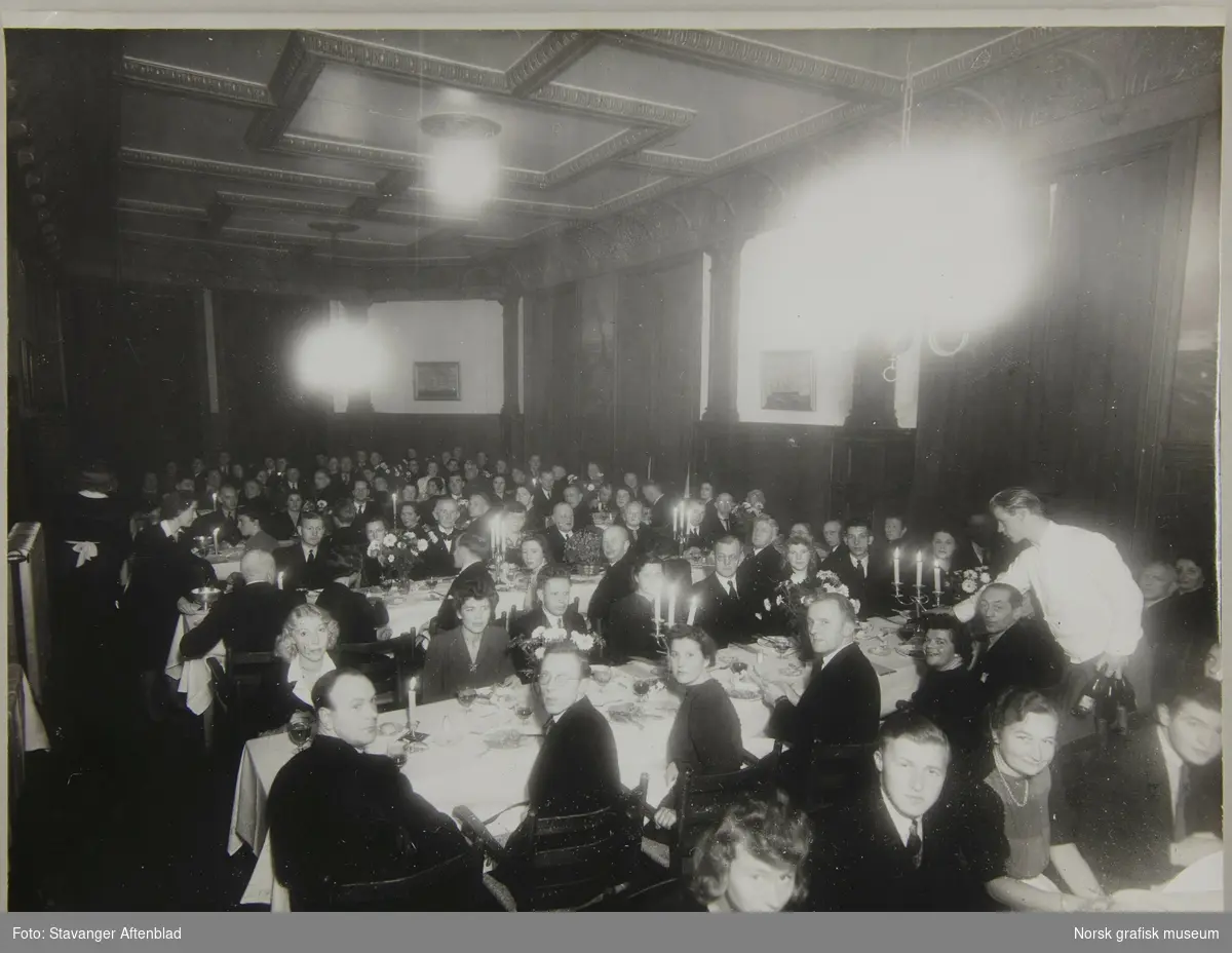 Middagsselskap i en stor sal, med et stort antall finkledde mennesker tilstede.