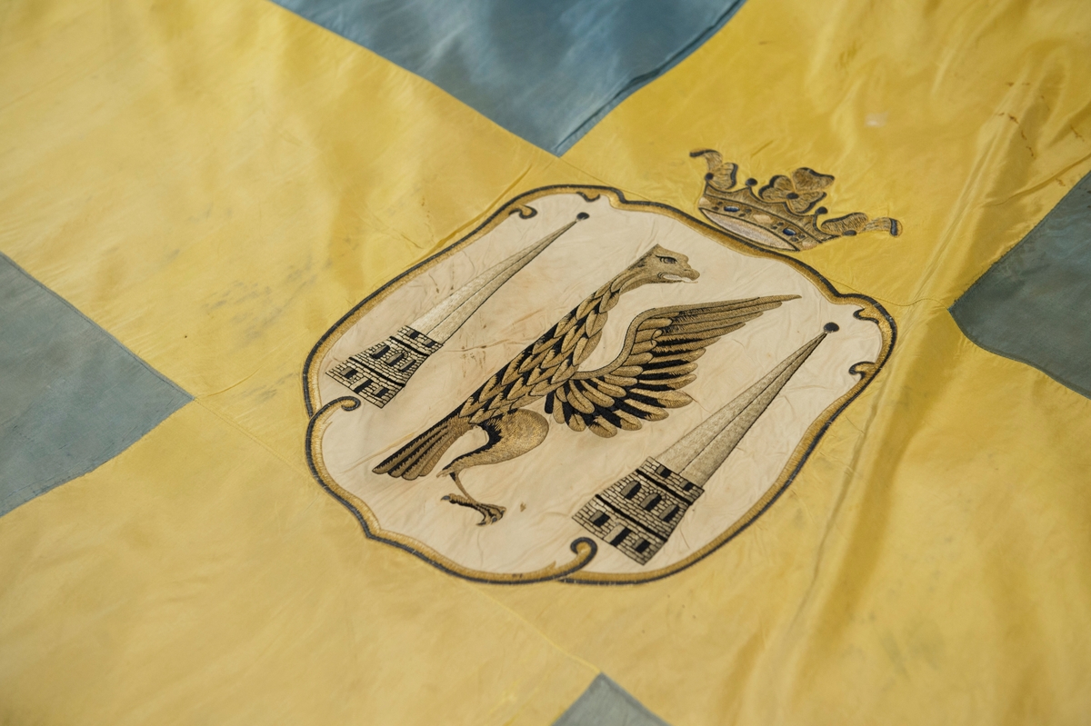 Fana av gult och blått natursiden, dubbet tyg, med heraldiskt motiv: Karlstads stadsvapen. Motivet är placerat i mitten av det gula korset och består av en applikation av vitt siden med heltäckande broderi. Fanan är fäst på vitmålad stång med en fanspets i metall med Carl XV's namnskiffer. Runt skiffret en lyrformad lagerkrans, krönt med symbolen för det allseende ögat med strålar runt.