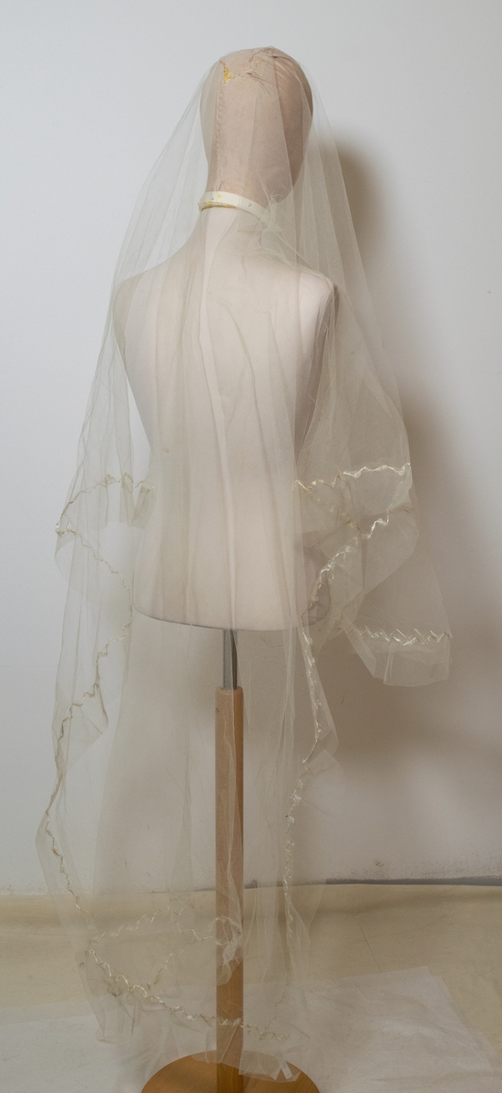 Hvit gjennomsiktig brudeutsyr av silke betsående av brudeslør, myrtekrans og kjolepynt.