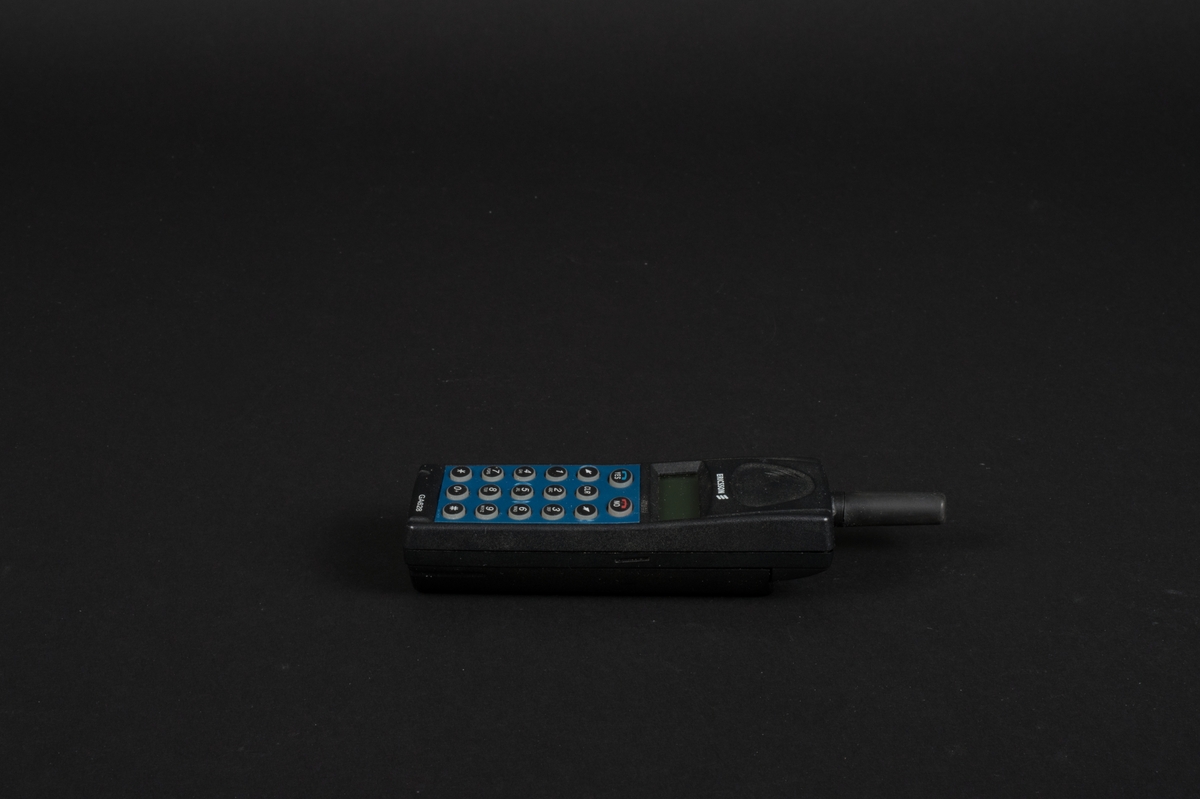 Mobiltelefon i svart plast med löstagbar blå frontpanel. Telefonen har en display och en antenn. Bakstycket utgörs av ett löstagbart batteri. Innanför bakstycket finns en simkortshållare.  Kontakt för laddare finns på telefonens undersida. Bredvid antennen sitter en lysdiod.