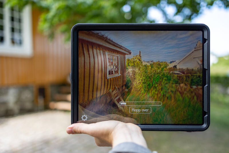 En ipad holdes av en hånd og viser et bilde av Munchs hus.