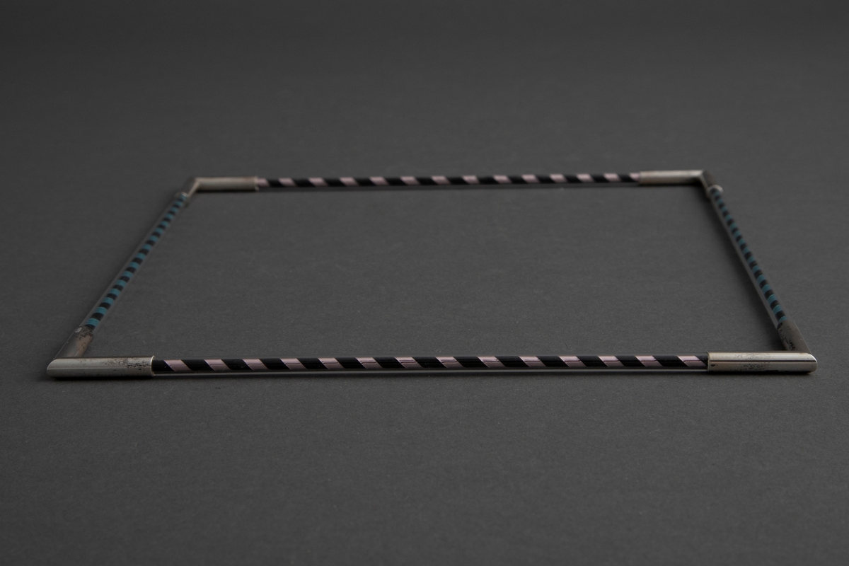 Halssmykke formet som et kvadrat der hver side består av en piperenser surret med metallbånd inni et plexirør. Hver side er knyttet sammen med sølvledd formet som to rør som møtes i rett vinkel. Se NK1985-039 for tilsvarende armsmykke.