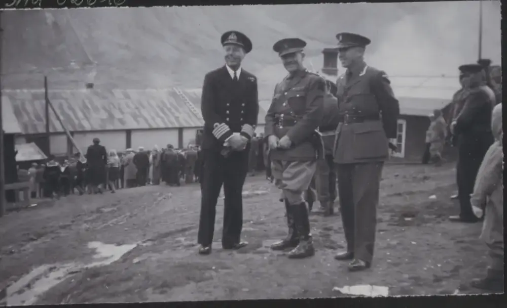 Tre menn i militæruniform. Kø av mennesker som evakueres i bakgrunnen.