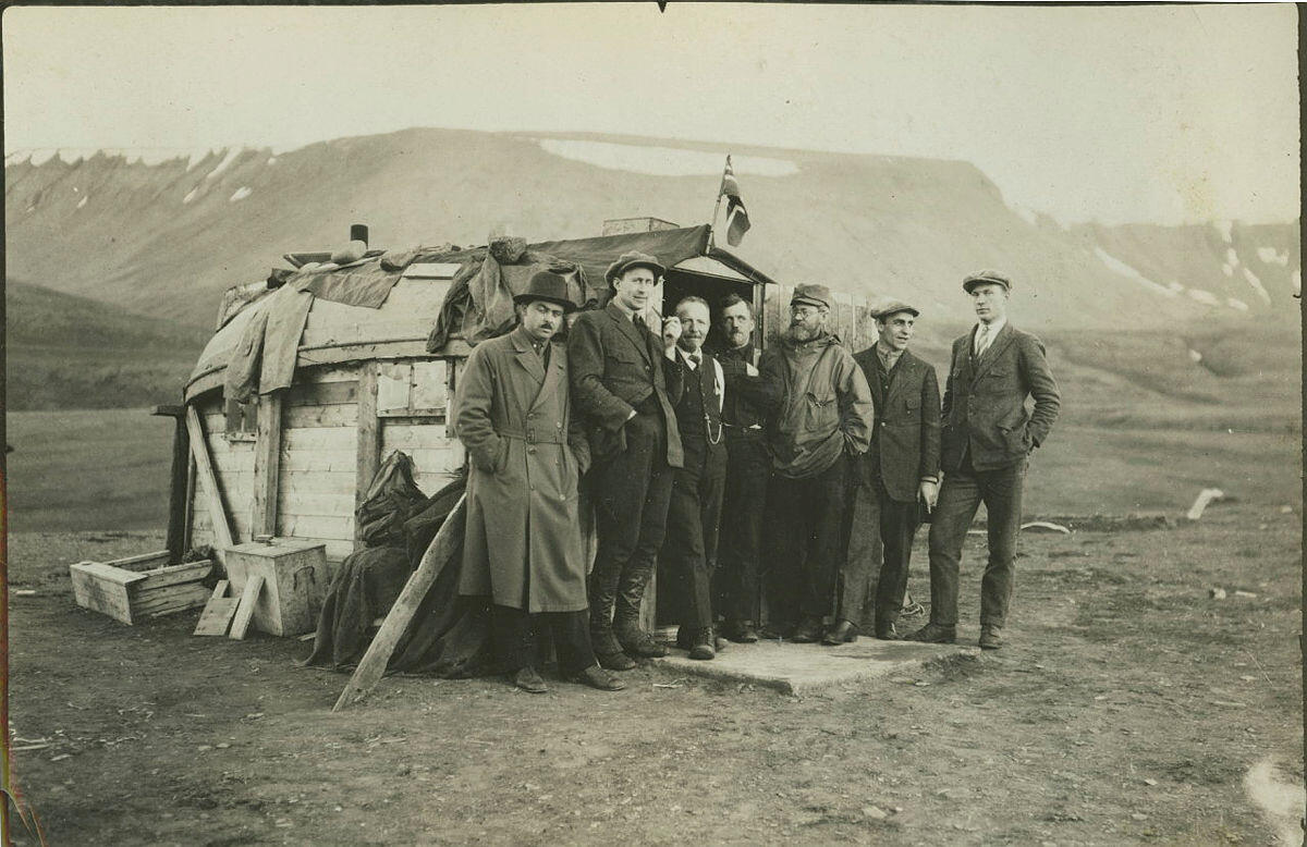 Bildet viser en gruppe menn foran en bistasjon, altså fangsthytte. Adolf Hoel har skjerf og anorakk.