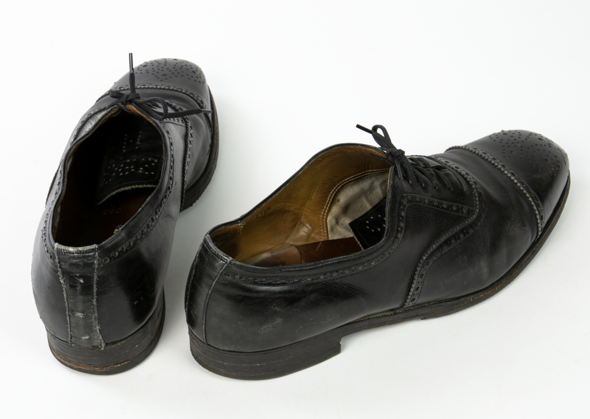 Ett par svarta lågskor av läder. Storlek H 290. Skohättorna är perforerade. Klack med gummisula.