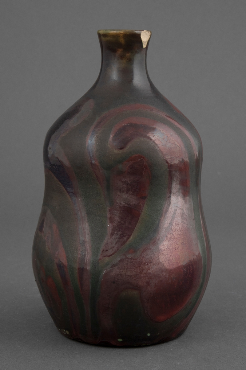Vase med matt lusterglasur. Glalsuren er i grønnlige toner, men noen partier i rødlige og fiolette toner, og noen i matt og svakt lustret grønn.