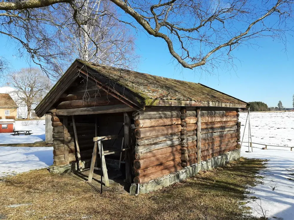 Bildet viser en eldre lintørke. Huset er laftet. Det er snø på bakken.