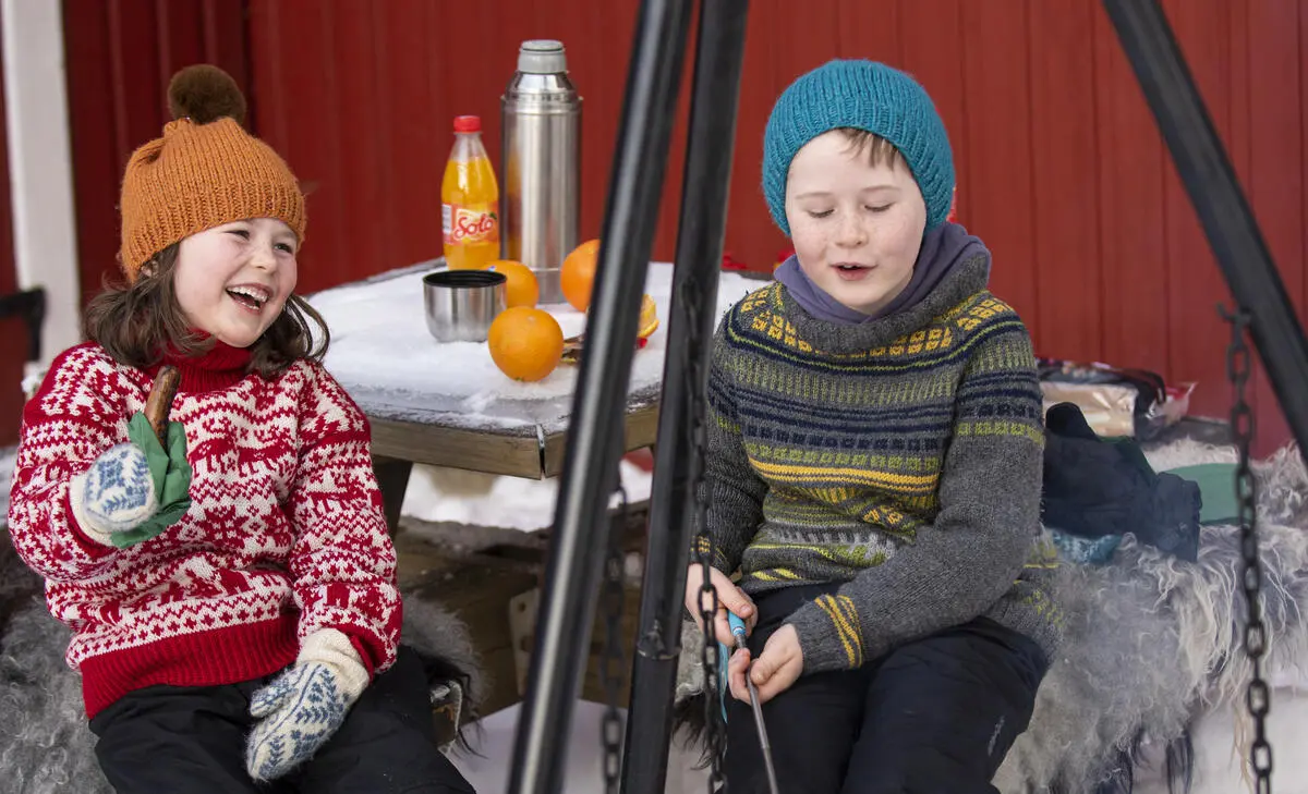Bildet viser to barn som sitter ute og spiser pølser i museumsparken