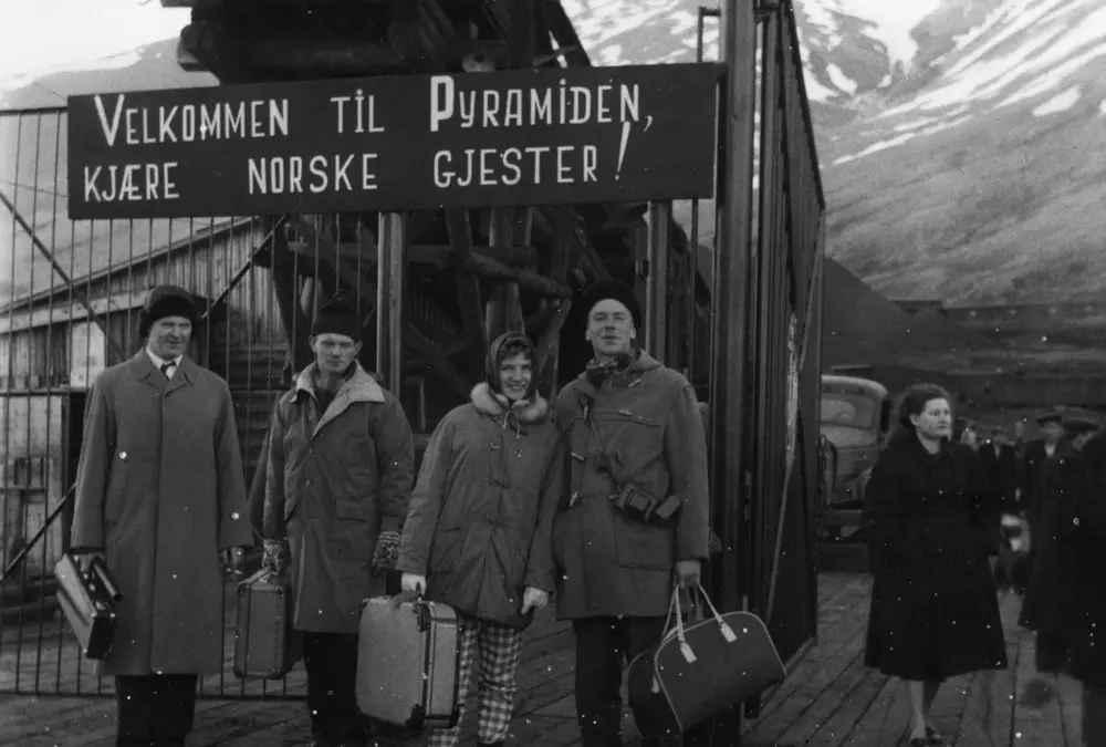 Picture of four people infront of a sign saying welcome to Pyramiden, dear Norwegian guests.