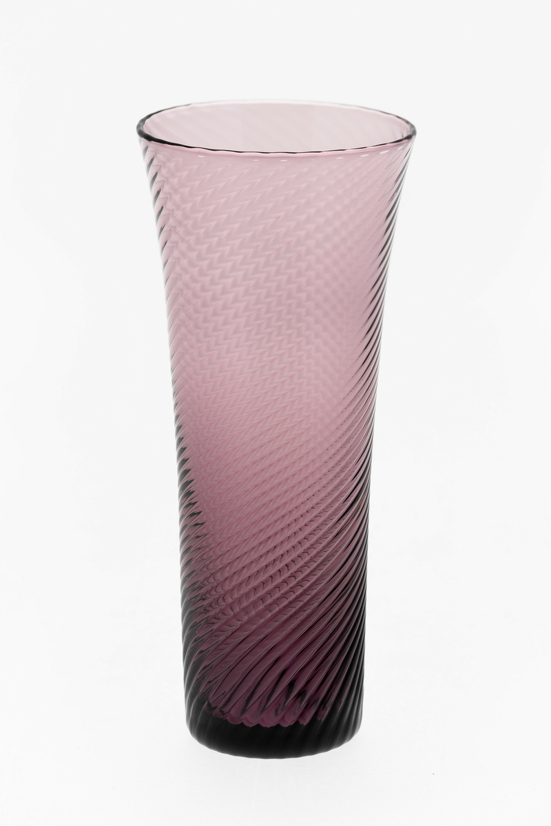 Seltersglass i purpurfarget gjennomskinnelig glass. Svak konisk form med sirkulær munningsrand, hvor spiralformede riller snor seg langs korpus.