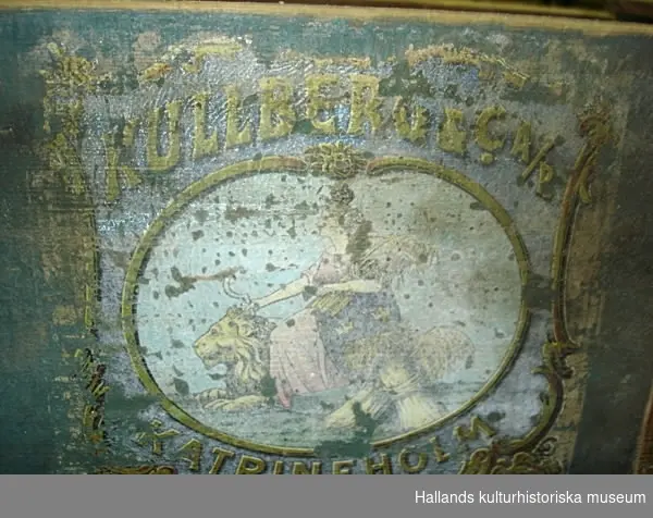 Maskin av trä och järn. Grönmålat. Text: "10/12 1917 MARIEHOLMS BRUK", "Katrineholm, Kullenberg AB", samt en bild av kvinna och lejon.