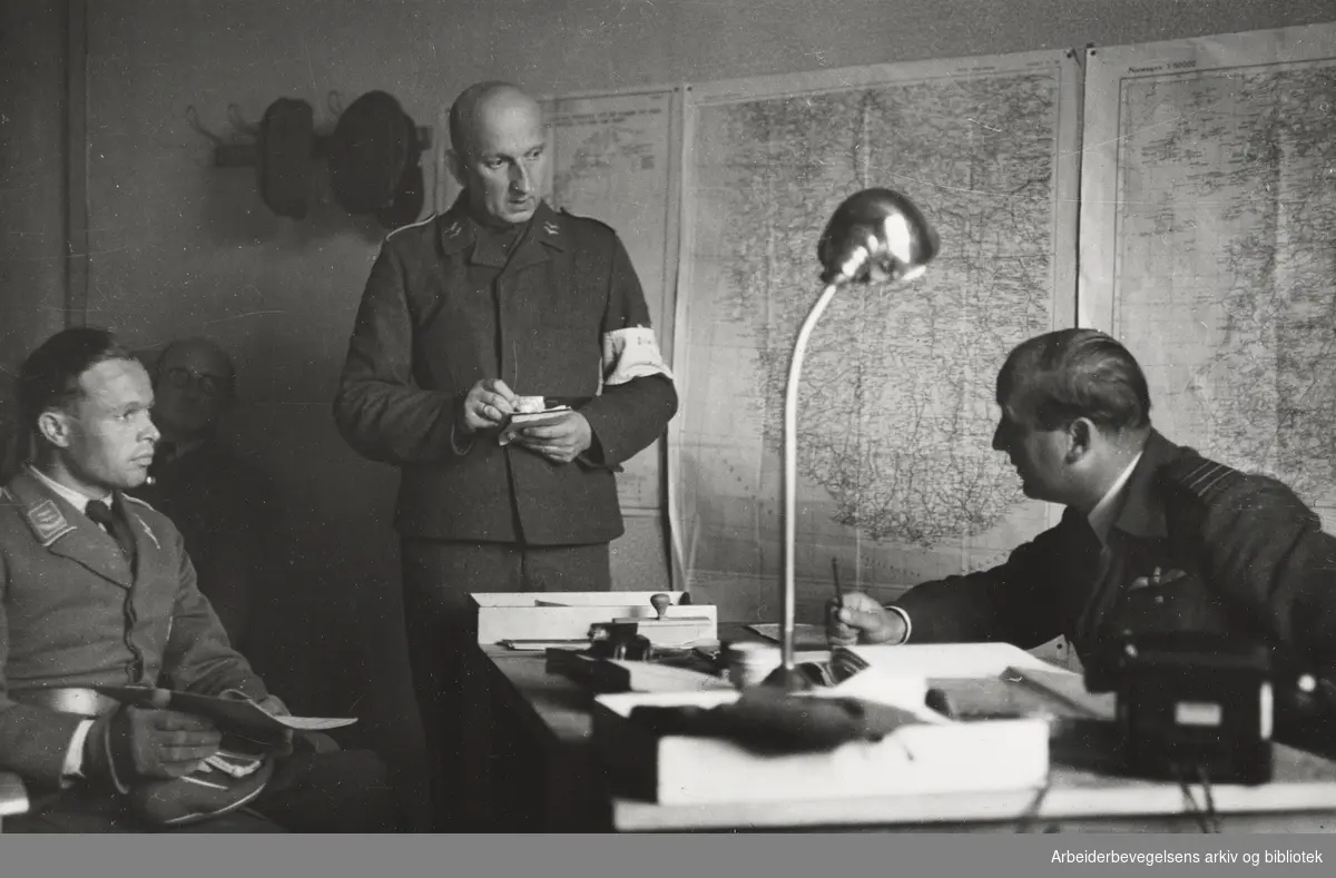Avvæpning av tyskere - fortsatt flere tusen tyske soldater i Norge. Wing Commander Russel fra britiske Royal Air Force og en offiser fra Luftwaffe i samtale på Sola flyplass. En tysk tolk tar instrukser og notater. August 1945