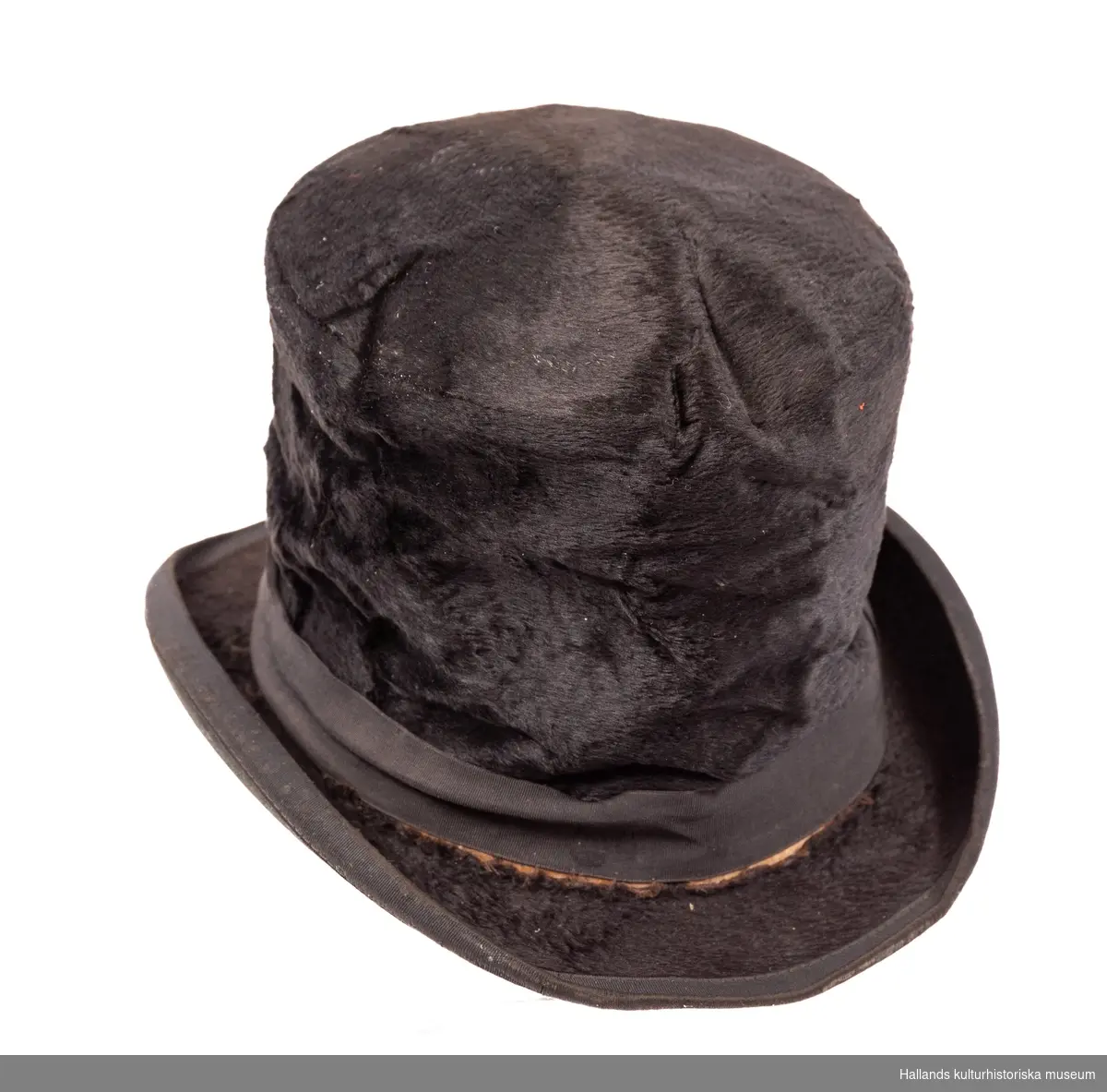 Hög hatt, klädd med svart silkesfilt och kanter med ripsband. Fabriksmärke "Best Quality". Mycket illa medfaren.