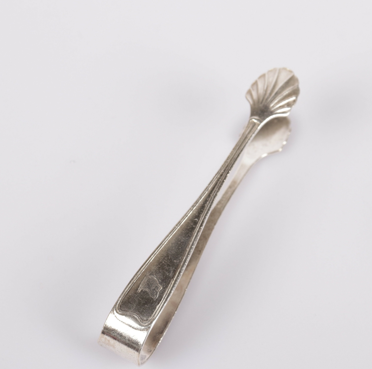Sukkerklype i sølvplett med et vifte mønster på selve  klypehodet. Rederiflagget til VDS er stemplet inn på den ene siden.