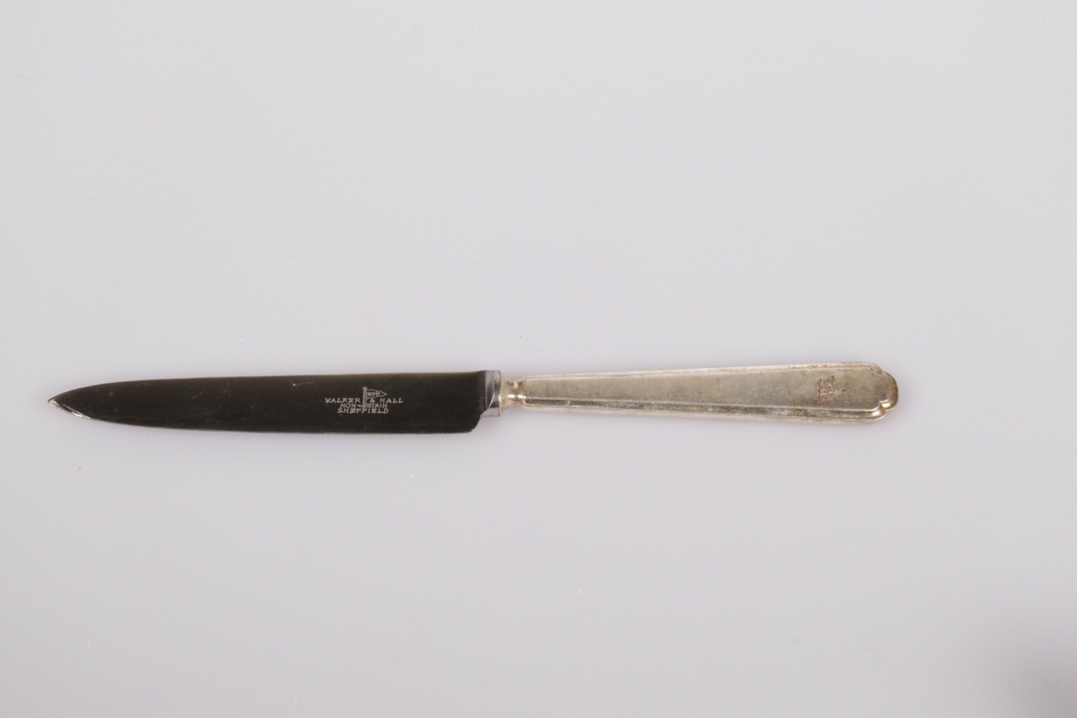 Knivbladet har en spiss odd. Rederiflagget til Det Bergenske Dampskibsselskab er gravert på enden av skaftet. Bladet og skaftet er laget i to forskjellige materialer.