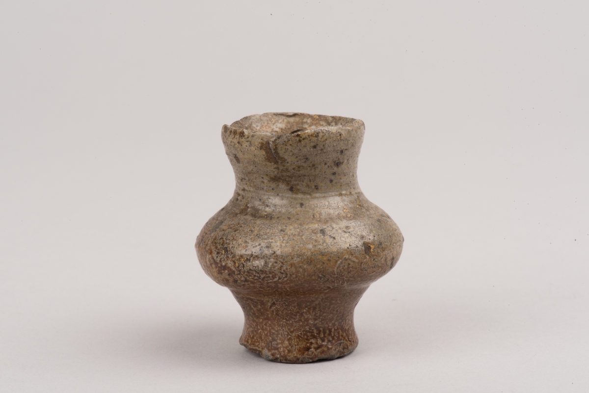 Ett så kallat salvekrus, ett miniatyrkrus av keramik, troligen stengods.
Runt, bukigt krus som smalnar av mot fot och mynning. Från mynning och ned till den bukigaste delen på kruset sitter ett öra.