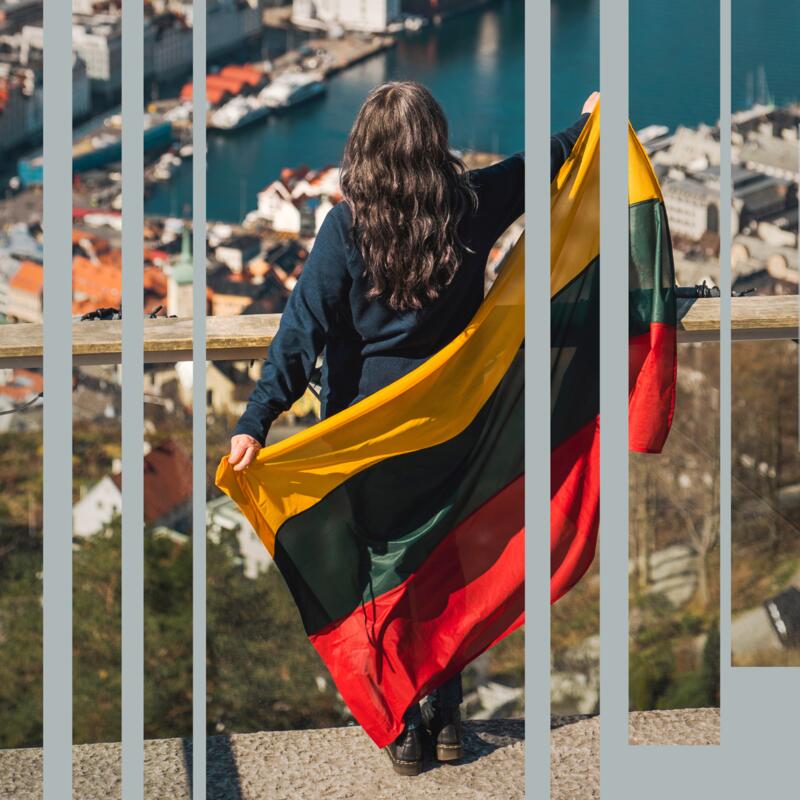 Kvinne, sett bakfra, holder latvisk flagg og speider utover Bergen fra Fløyen