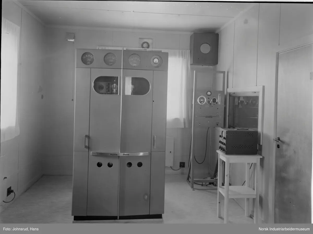 Interiør relestasjon for Notodden Kringkaster. Western Electric maskin stående midt i rommet.