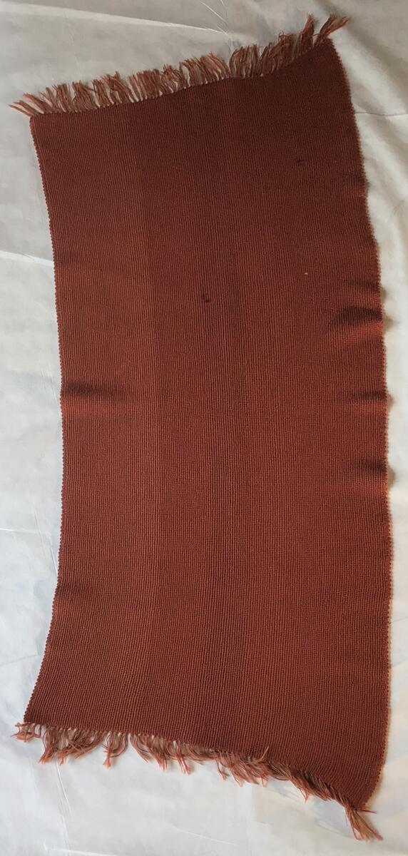Stolteppe i vevd ull. Den er orange og brun med buet form.