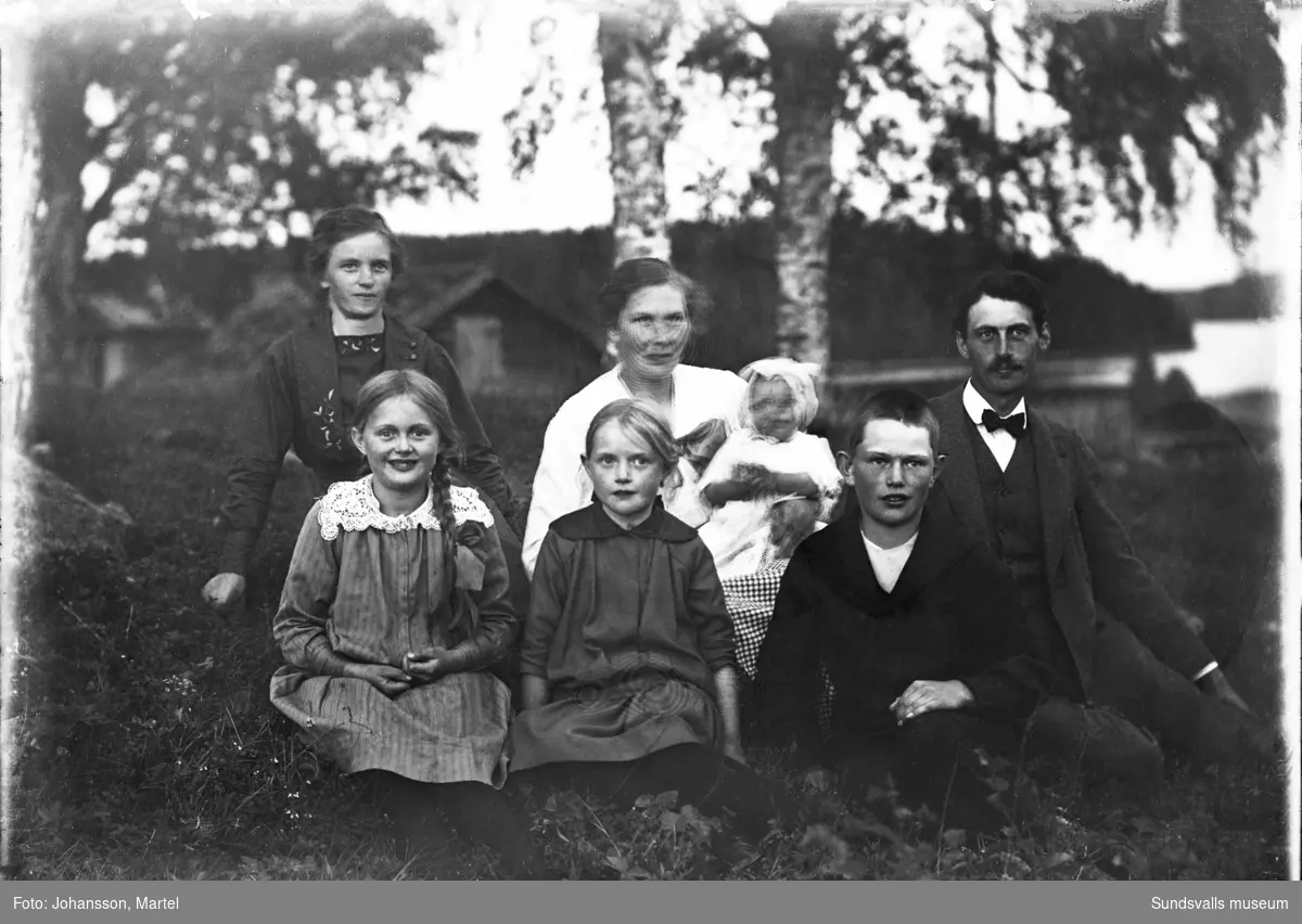 Familjeporträtt i det gröna, föräldrar och fem barn i olika åldrar. Fotograferat från Skedvik i Attmar, söderut över Vikarn med Häggeberget i bakgrunden.