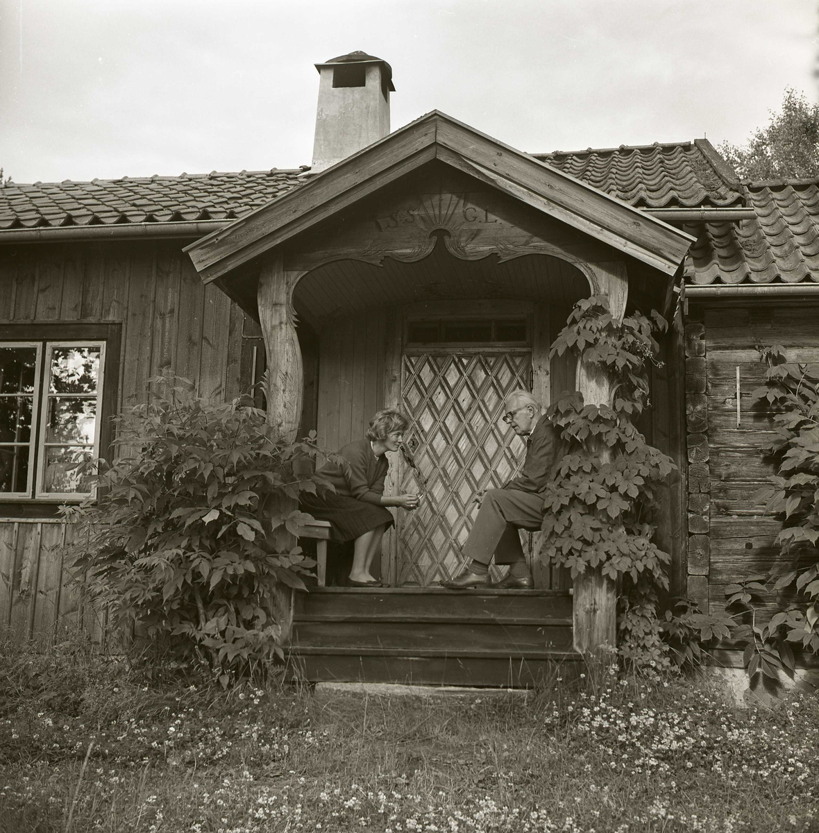 En man och en kvinna sitter på förstukvisten framför en sommarstuga i Undersvik, 1966.