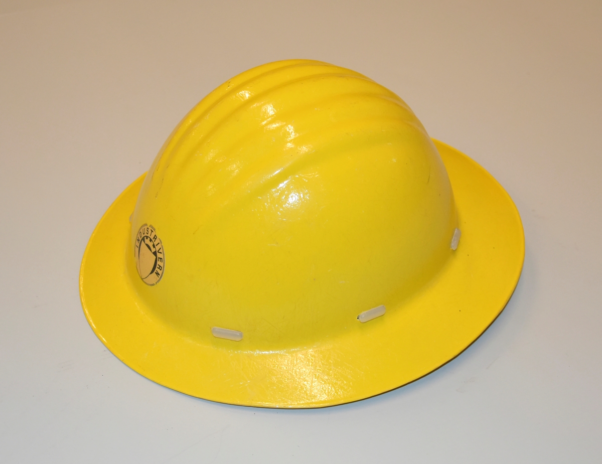 Hjelm i gul plast. Innmaten er laget av plast. Med Industrivern-logo.