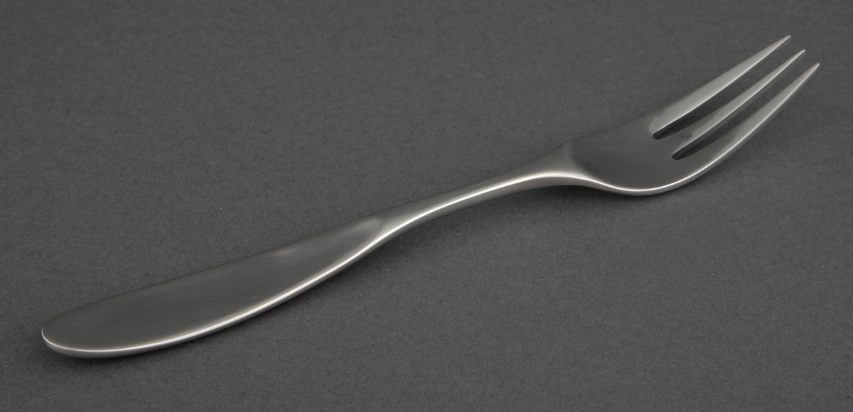 Spisegaffel i presset rustfritt stål med smalt, ovalformet gaffelblad med tre lange tinner, smal skaftrot og smalt, ovalformet skaft med avrundet ende.