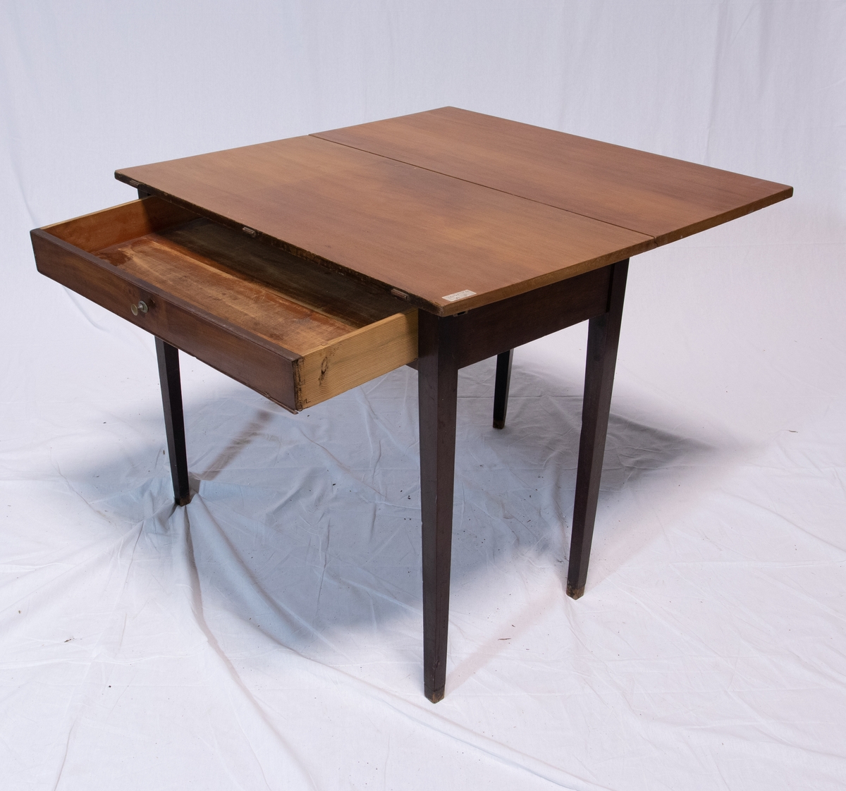 Todelt spisebord bestående av to nesten like rektangulære brune bord med en hengslet rektangulær vinge hver. Det ene bordet har skuffe.