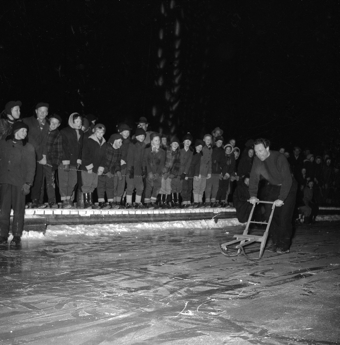 Serie bilder med munter vinterlek, uppvisningar och musik. Vintern 1955 arrangerade Pressfotografernas Klubb en isfest i Tinnerbäcksbadet i Linköping. Omväxlande innehöll kvällen dragkamp, kanåkning, sparkstöttingsstafett och detsamma på skridskor, vid sidan av en kvalificerad uppvisning i konståkning. Efter showandet blev det dans för allmänheten där Jörgen Olsens orkester spelade med Yvette Guy som vokalist.