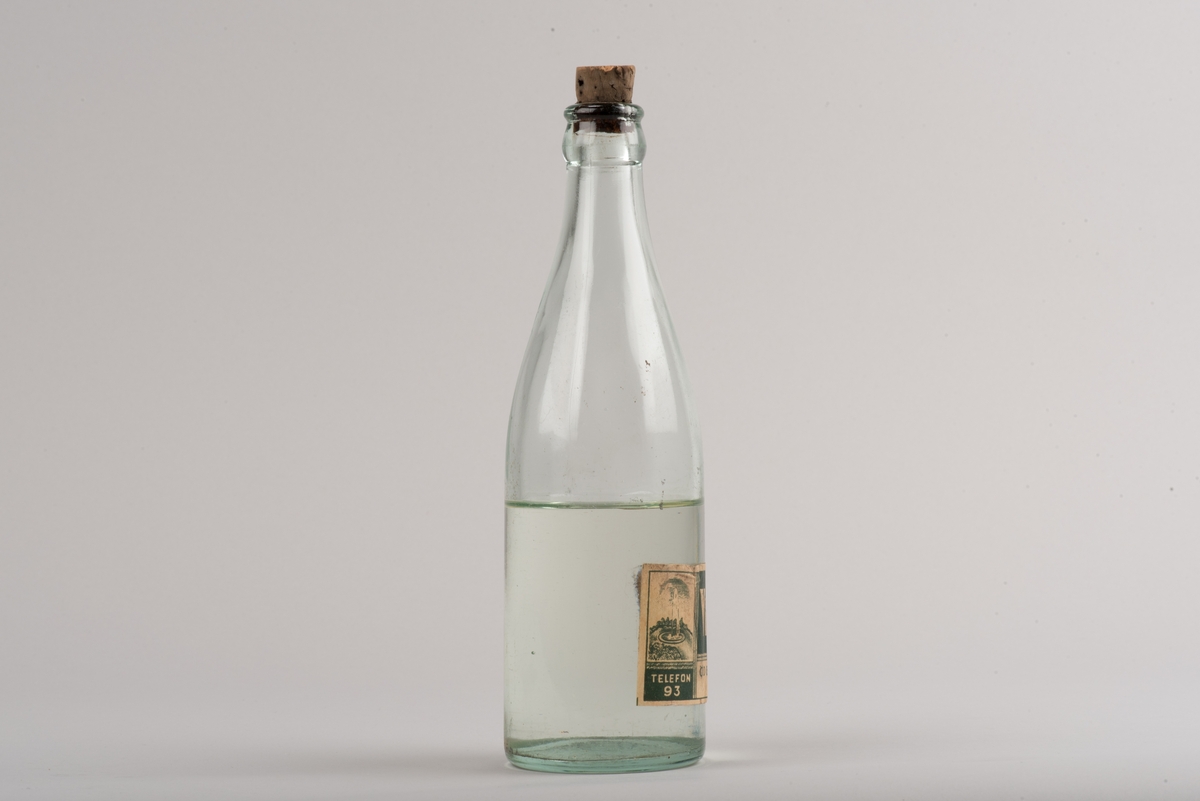 Flaska av klart glas med kork.
Glasflaska med avsmalnande hals. På flaskan finns ett inpräglat L och två stiliserade blommor.
På etiketten framgår det att den tillverkats för vichyvatten i Ödeshög. Numera innehåller flaskan olja.